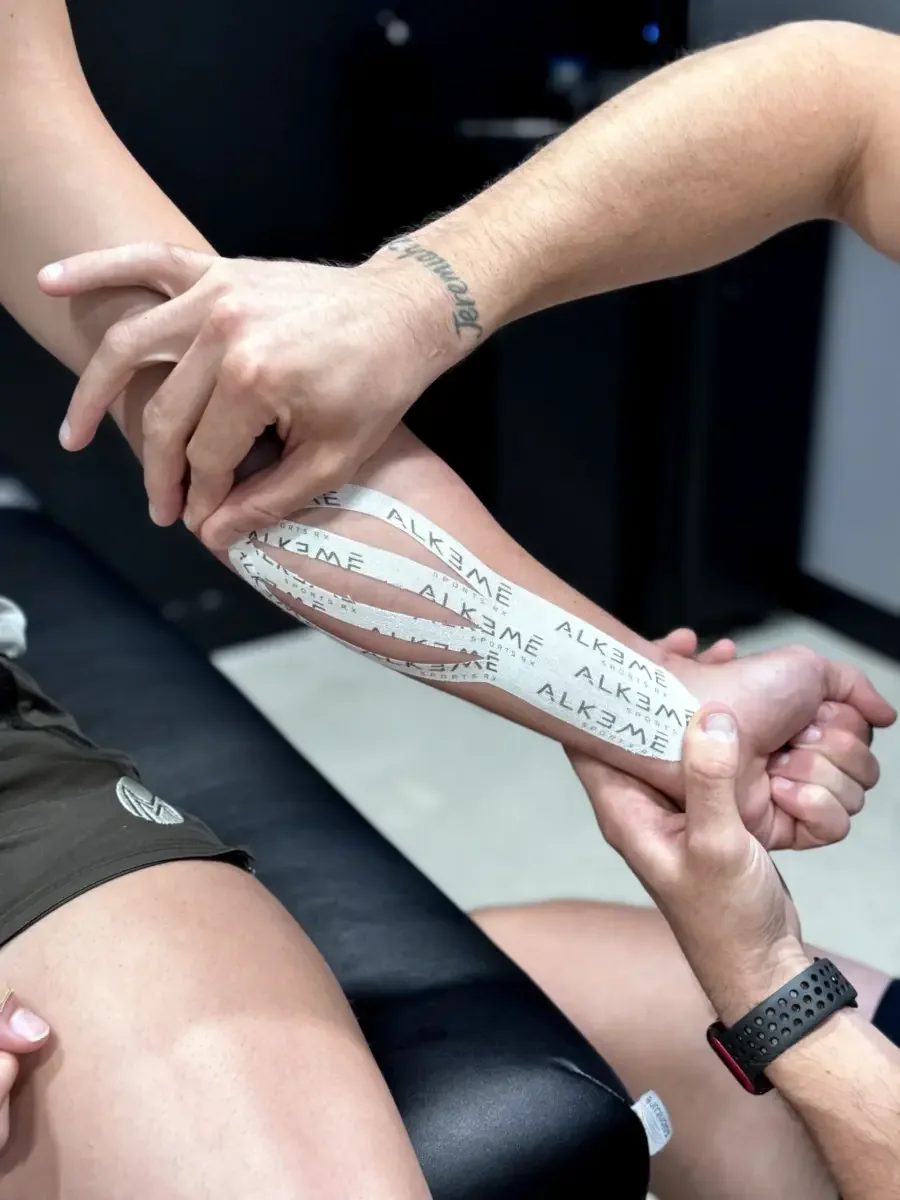 A Doctor of Physical Therapy applying kinesio tape to an athlete's shin at Alkemē Sports Rx in Davie, FL