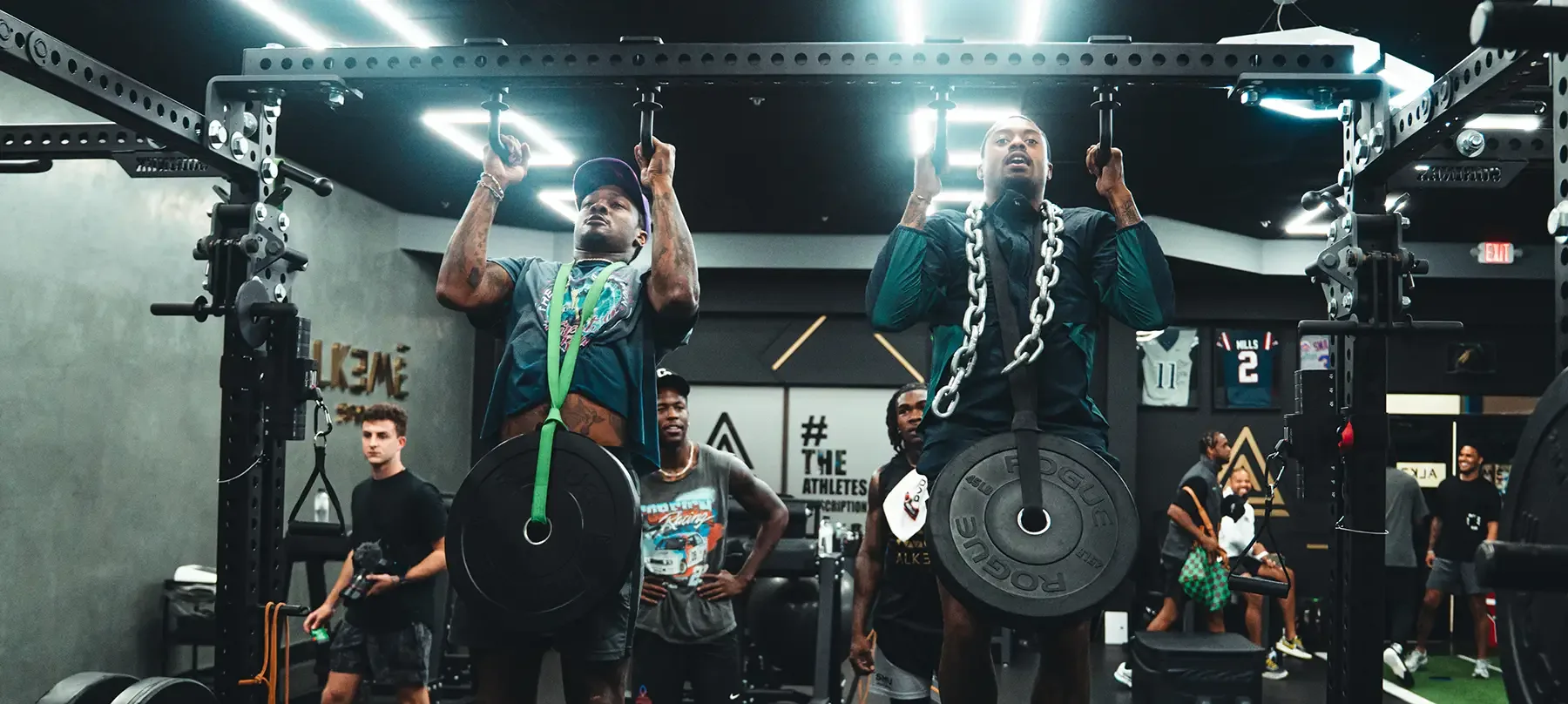 Two athletes pulling weighted chin-ups in the rack at Alkemē Sports Rx in Davie, FL