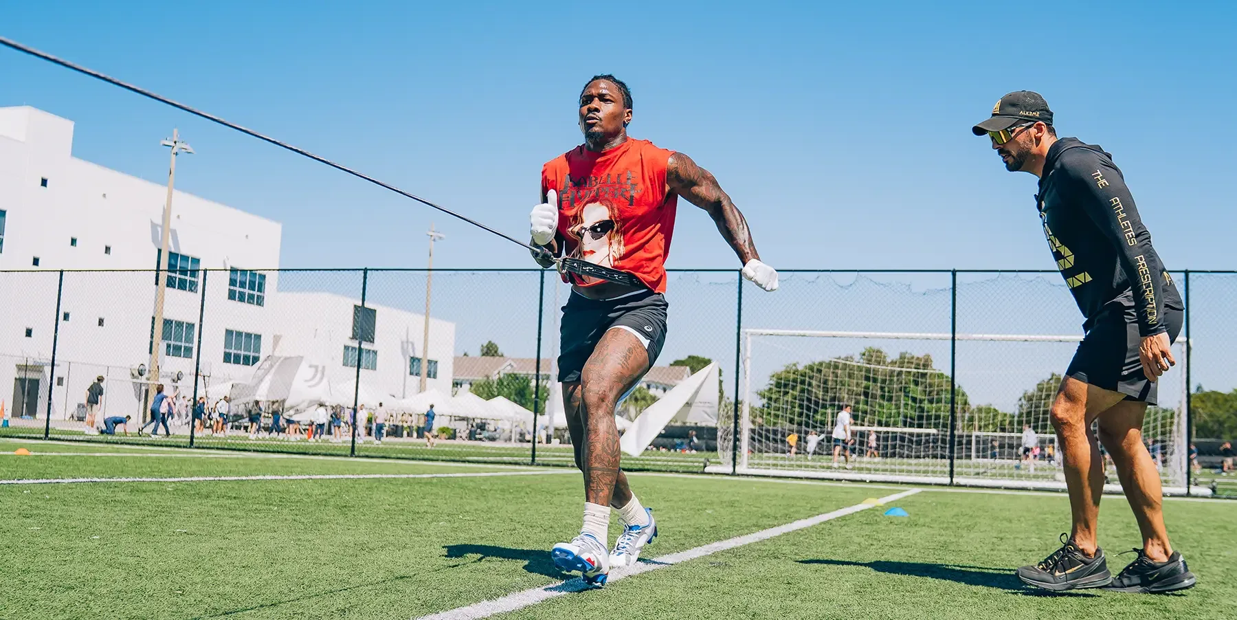 A coach watching an athlete through resisted sprint work on the field at Alkemē Sports Rx in Davie, FL