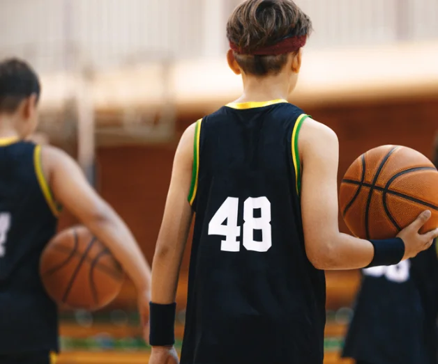 Young basketball player wearing jersey number 48, holding a basketball, with teammates in the background, emphasizing youth sports training and injury prevention.